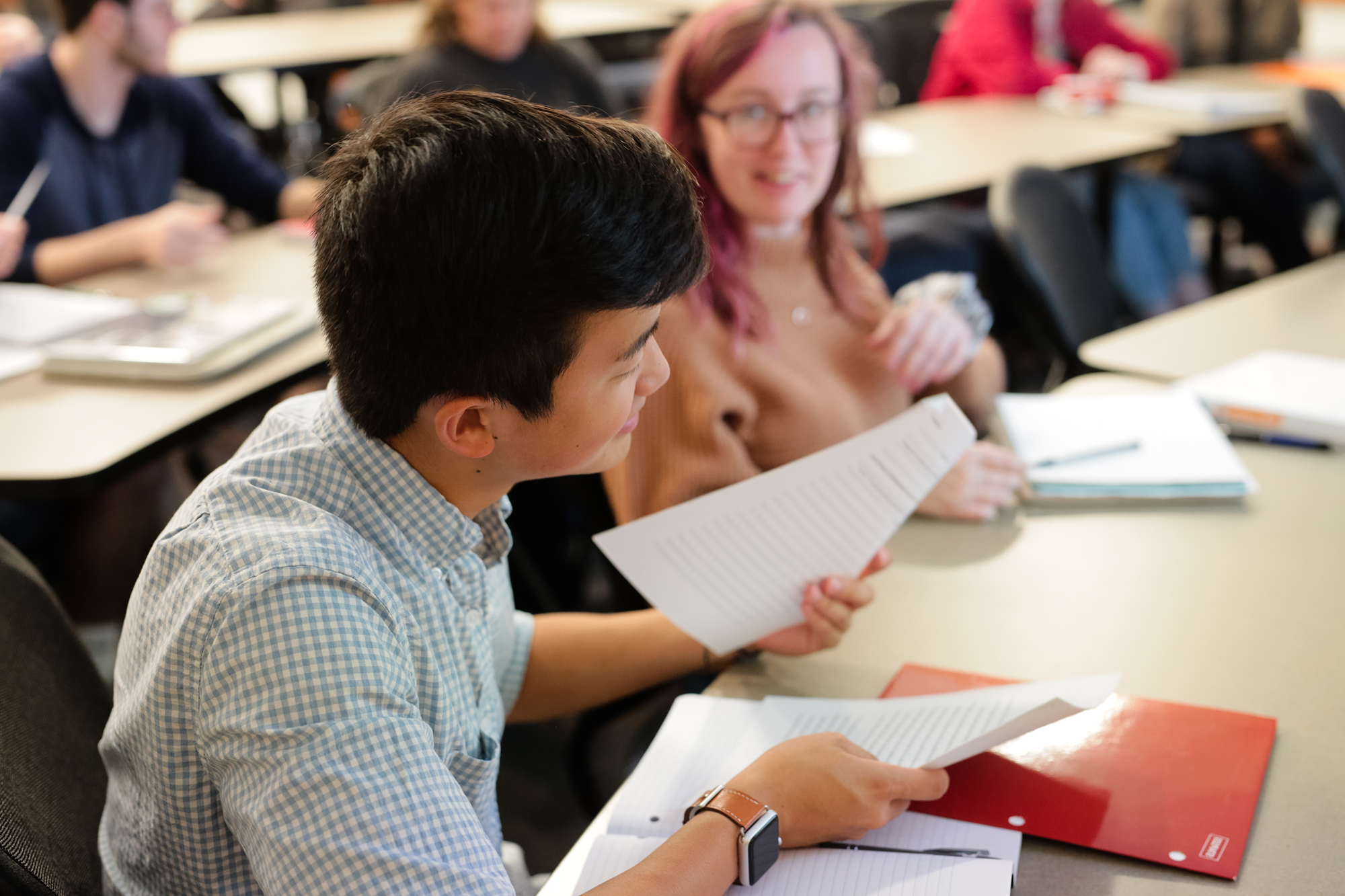 Male student holding a piece of paper and sitting in a classroom.